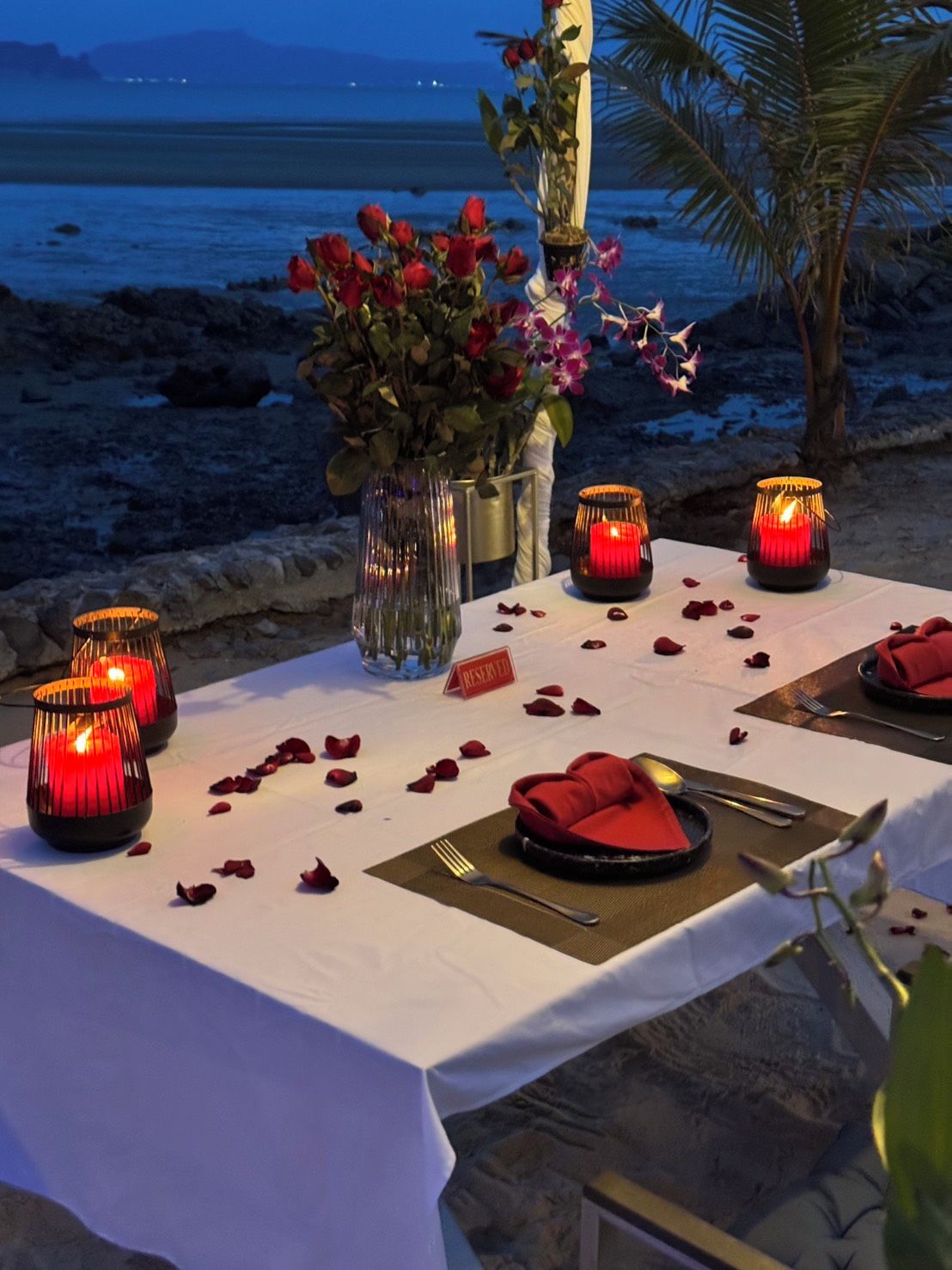 Un montaje para cenar al aire libre con velas, una mesa para dos y vista al océano.