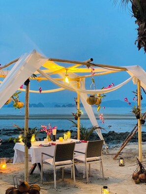 A beachside dining setup with a table under a canopy, surrounded by chairs, and decorated with flowers and candles. - Saengsuree Villas Koh Yao Yai (Koh Yao)