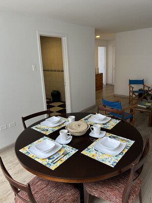 Un comedor con una mesa redonda dispuesta para cuatro personas, rodeada de sillas con cojines de asiento trenzados.