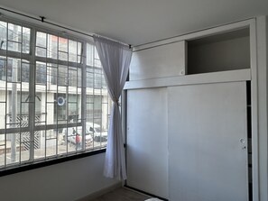 A room with a large window, a white wardrobe, and a view of the street outside. - New Listing (Bogotá)