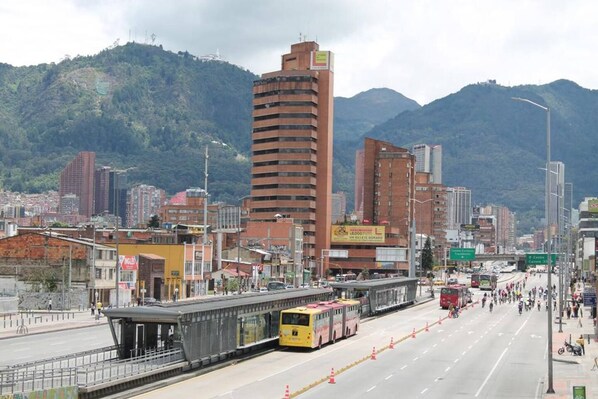 Un paisaje urbano con un edificio alto destacado, una parada de autobús y una calle con vehículos.