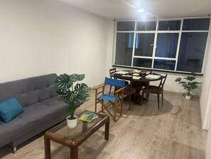 Ein Wohnzimmer mit einer Couch, einem Couchtisch, einem Esstisch mit Stühlen und einem großen Fenster.