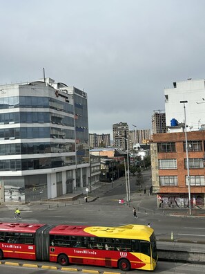 Une rue de la ville avec un autobus rouge et jaune, des immeubles et un ciel dégagé.