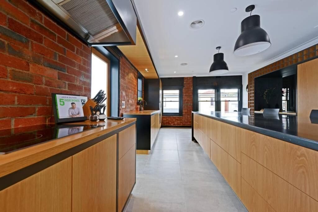 A modern kitchen with wooden cabinets, a brick wall, and pendant lighting.