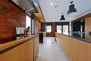 A modern kitchen with wooden cabinets, a brick wall, and pendant lighting. - Designer Living in Historic Art Deco (Hobart)