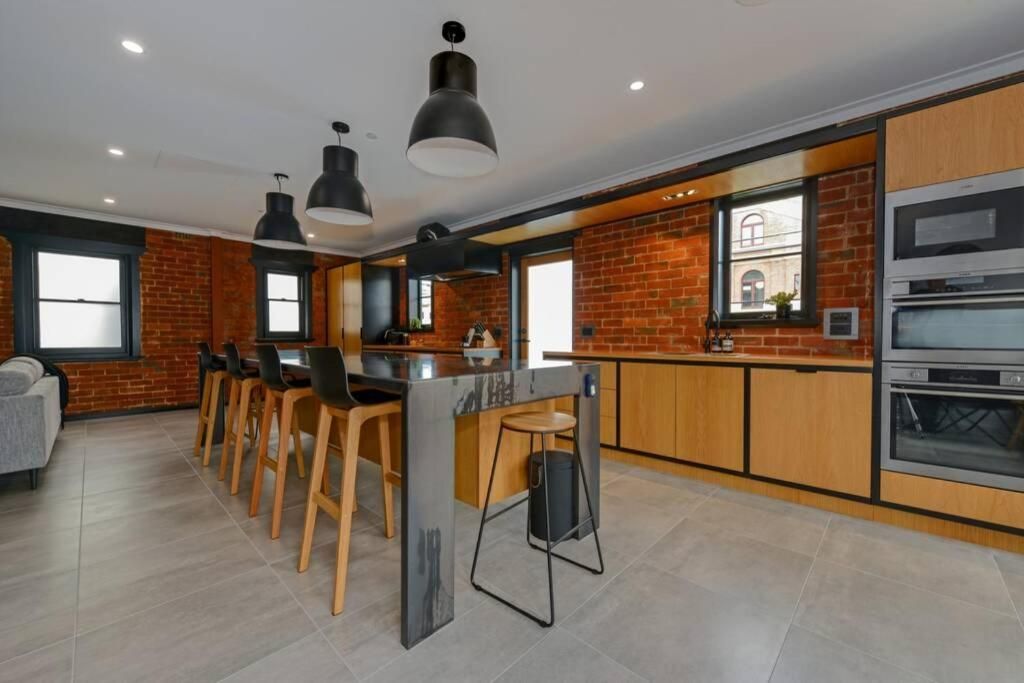 A modern kitchen with a brick wall, wooden cabinets, a bar area with stools, and built-in appliances.