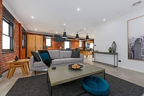 A modern living room with a sofa, coffee table, and a cityscape painting. - Designer Living in Historic Art Deco (Hobart)