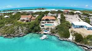 A coastal property with a large house featuring a swimming pool, a boat docked in the water, and a clear view of the ocean. - Alta Bella Villa 8 Bdr Oceanfront Nordic Spa (Providenciales)
