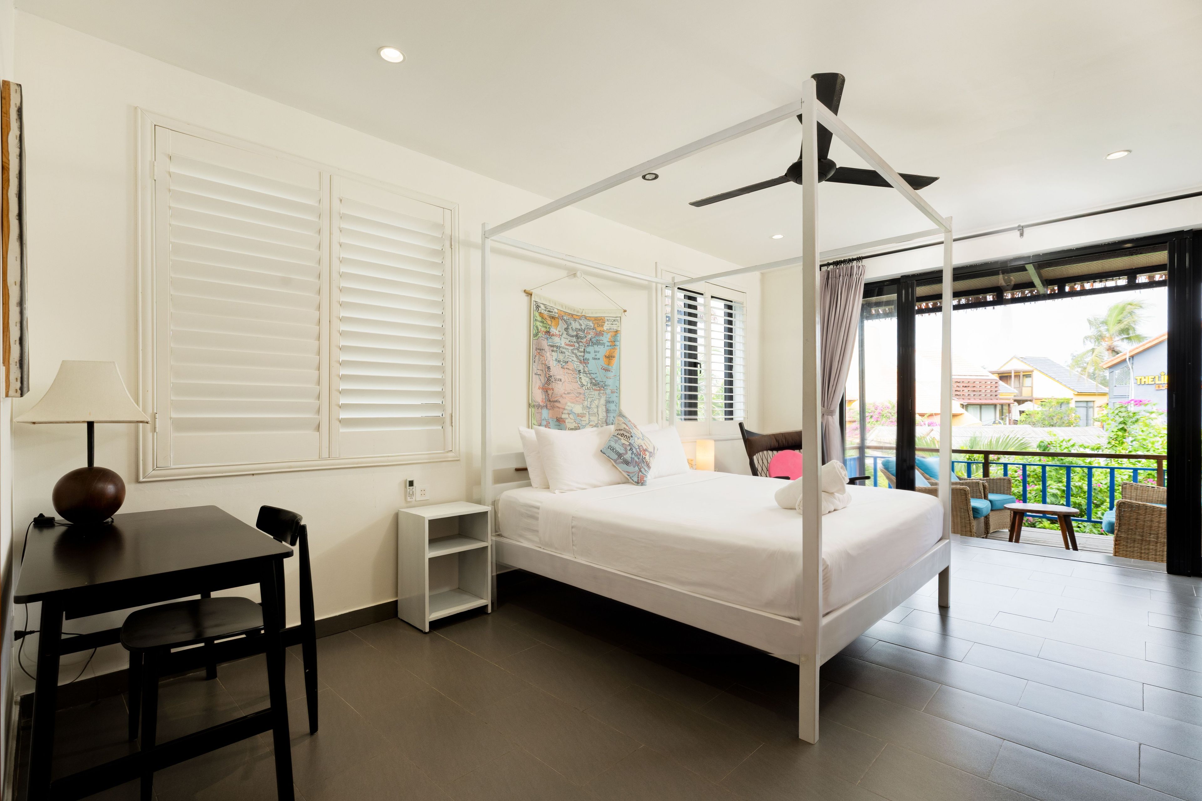 Een hotelkamer met een hemelbed, een kaart aan de muur, een balkon met zitplaatsen buiten en een tafel met een lamp.