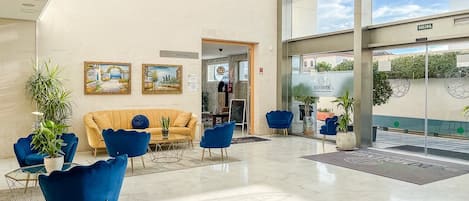 Um lobby moderno com um sofá amarelo, cadeiras azuis e entrada de vidro.