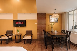 A room with a dining table, chairs, a TV displaying 'NETFLIX', a potted plant, and a brick wall. - OH Trendy homes Hoan Kiem LTT - City view duplex (Cua Nam)