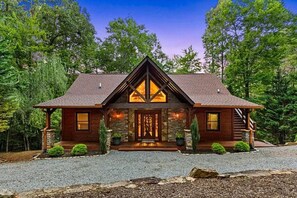 A log cabin with a stone foundation, a steeply pitched roof, and a front porch with a staircase leading to the entrance.