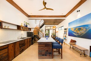A modern kitchen with wooden cabinetry, a central island, and a dining area with blue chairs. - Sea Easter Villa 3BR Beachside An Bang Beach Hoi An by Beachside Boutique Homes (Đà Nẵng)
