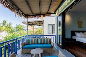 A balcony with a wicker sofa, a small round table, and a bed with white bedding. - Sea Easter Villa 3BR Beachside An Bang Beach Hoi An by Beachside Boutique Homes (Đà Nẵng)