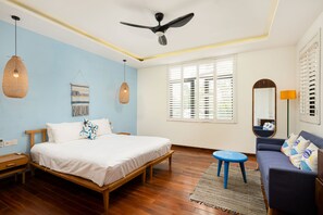 Ein Schlafzimmer mit einem Bett, einem blauen Sofa, Holzboden, einem Deckenventilator und einem Fenster mit Jalousien.