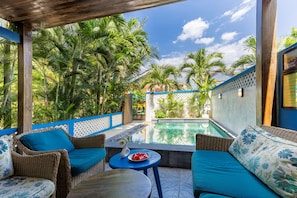 A poolside area with wicker furniture, a small table with a watermelon, and a view of a building with a sign. - Sea Easter Villa 3BR Beachside An Bang Beach Hoi An by Beachside Boutique Homes (Đà Nẵng)