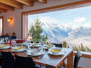 Mesa lista con platos, vasos y cubiertos, con vistas a un paisaje montañoso.