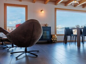 Ein modernes Wohnzimmer mit einem Ledersessel, einem Holzesstisch mit Stühlen, einem Schrank und einem großen Fenster mit Blick ins Freie.