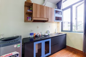 A kitchen with wooden cabinets, a black countertop, and a window with a view of buildings. - Comfortable Studio Kingbed Windows Mango Mango Apartments (Đà Nẵng)
