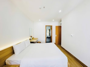 Hotellihuone, jossa on sänky, yöpöytä, peili ja puinen ovi.