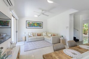 Ein modernes Wohnzimmer mit einem weißen Sofa, einem Esstisch und einer Uhr sowie einem Deckenventilator.