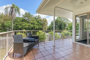 Ein Balkon mit einer Rattan-Couch und einer Glastür zu einem Innenbereich.