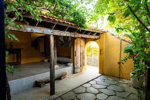 Eine rustikale Außenpatio mit Ziegeldach, Steinböden und einem hölzernen Bogen, der zu einer gelben Wand führt.