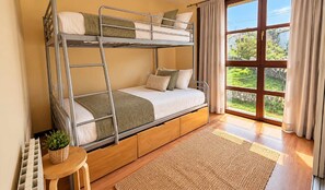 A bunk bed with a wooden platform, a small table with a plant, and a view of greenery through a window. - Villa Maruja: House with a Garden Near the Beach in Llanes (Llanes)