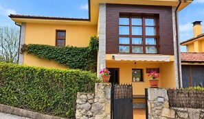 A two-story house with a yellow facade, a stone wall entrance, and a wooden fence. - Villa Maruja: House with a Garden Near the Beach in Llanes (Llanes)