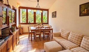 A dining area with wooden furniture, a large window with a view of greenery, and a painting on the wall. - Villa Maruja: House with a Garden Near the Beach in Llanes (Llanes)