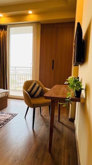 Et værelse med sofa, spisebord, fjernsyn ophængt på væggen og en skydedør, der fører ud til en balkon.