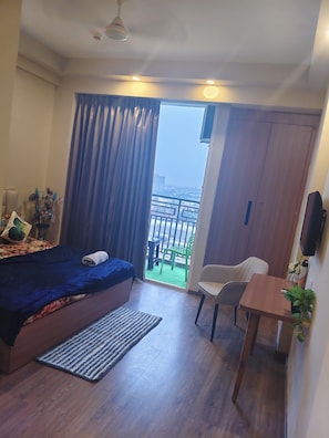 Et soveværelse med seng, skrivebord, stol, fjernsyn og udsigt til en balkon med gelænder.