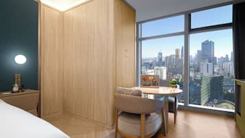 Habitación de hotel con vista a la ciudad, una cama, un escritorio y una pequeña mesa con una silla.