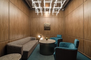 A room with a wooden paneled wall, a cushioned bench, a round table with a vase, and a blue chair. - Crystal Orange Hotel (Wuhan)