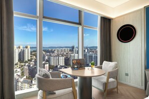 A modern room with a panoramic city view, a round table, two chairs, and a decorative wall piece. - Crystal Orange Hotel (Wuhan)
