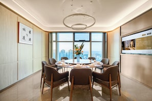 A modern conference room with a round table, chairs, a chandelier, and a large window with a city view.