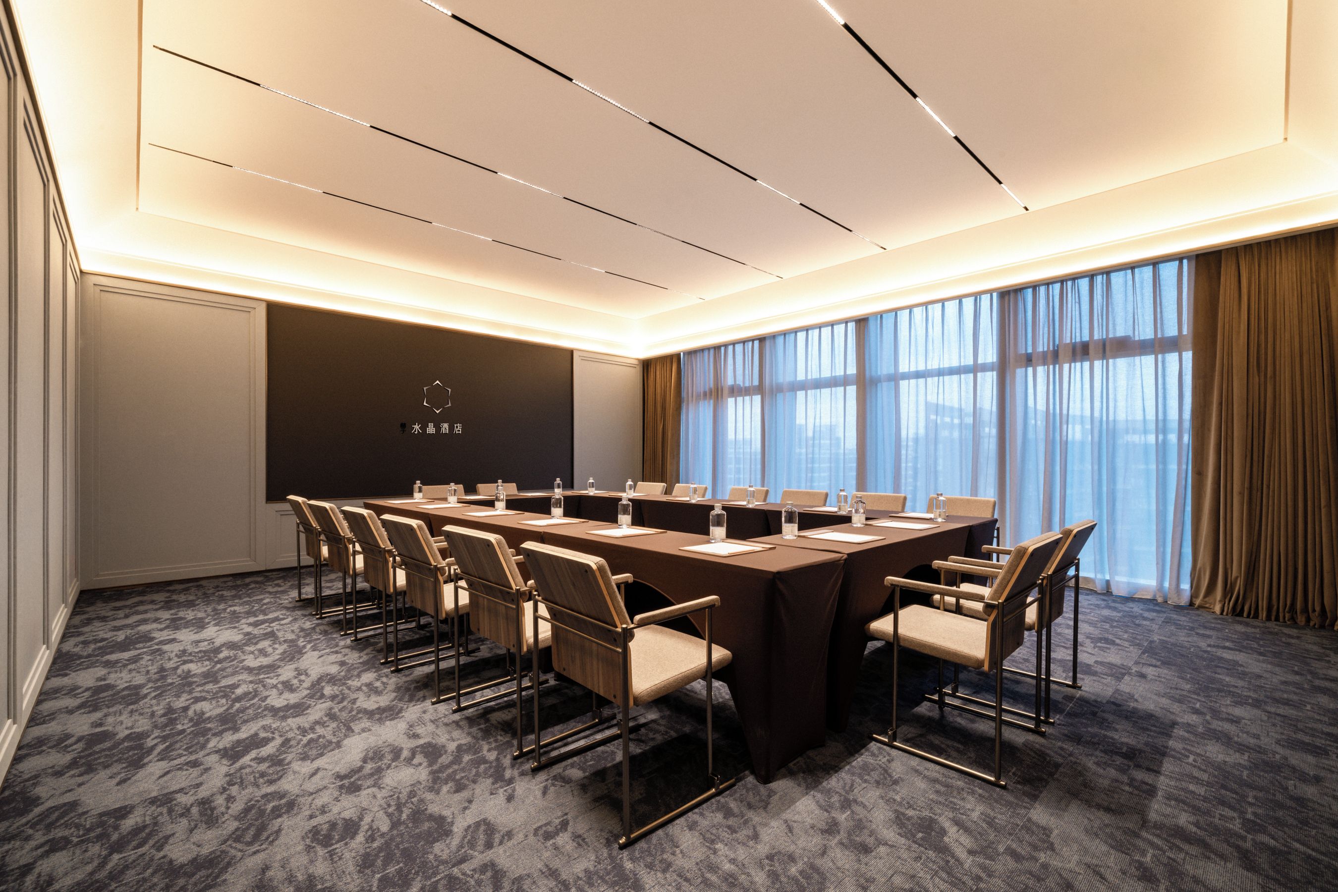 A conference room with a long table, chairs, and a large window with curtains.