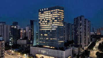A modern hotel with a prominent glass facade, surrounded by high-rise buildings in a cityscape.