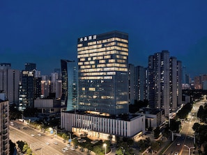 A modern hotel with a prominent glass facade, surrounded by high-rise buildings in a cityscape.