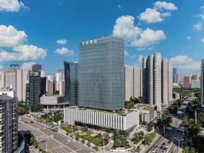 A modern hotel with a glass facade, surrounded by high-rise buildings and a clear blue sky. - Crystal Orange Hotel (Wuhan)