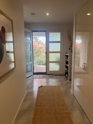 A hallway with a large glass door leading outside, a rug on the floor, and a white wardrobe. - Your Comfortable, Spacious Phillip Island Getaway (Cowes)