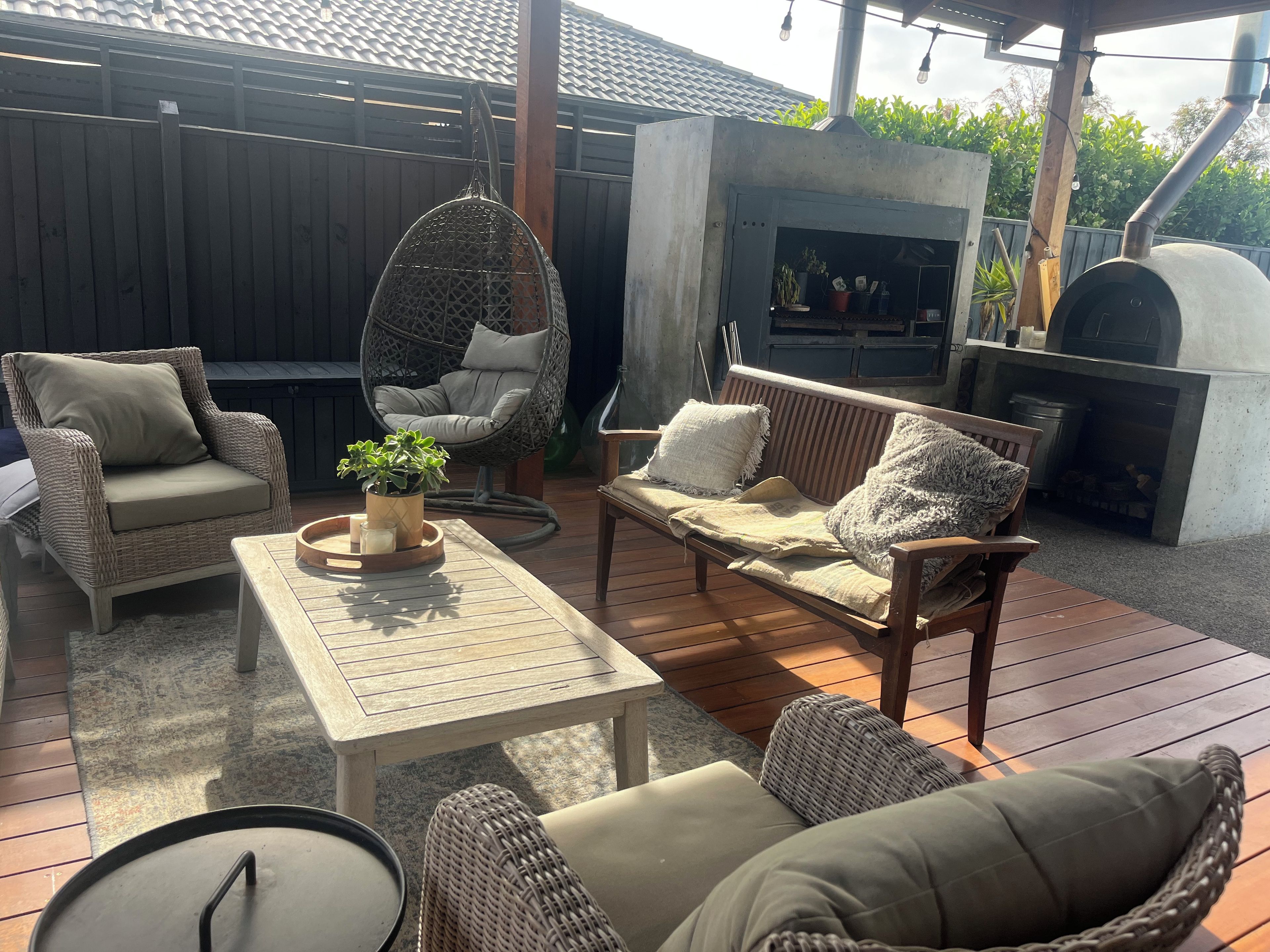 An outdoor patio with wicker furniture, a hanging chair, a table with a candle, and a built-in grill.