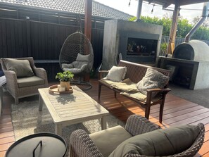 An outdoor patio with wicker furniture, a hanging chair, a table with a candle, and a built-in grill. - Your Comfortable, Spacious Phillip Island Getaway (Cowes)