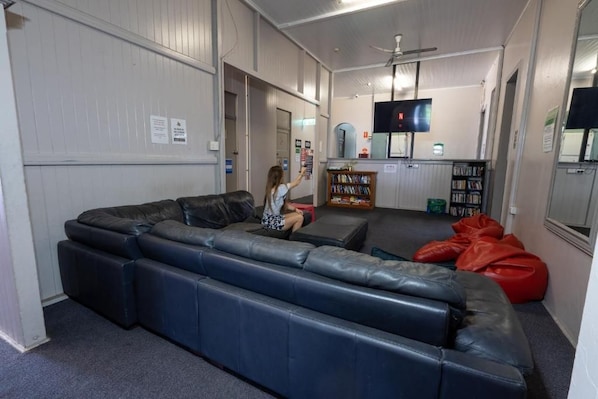 A room with a large black leather sofa, a red bean bag, and a television on the wall. - The Jack Backpackers (Cairns)