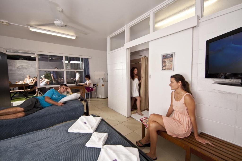 A hotel room with a bed, a bench, a TV, and a bathroom visible through an open door.