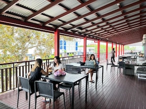An outdoor covered area with tables and chairs, a person walking, and a view of buildings in the background. - The Jack Backpackers (Cairns)