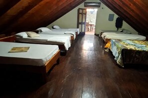 Un dormitorio con cuatro camas dispuestas en fila, suelo de madera y una puerta que da a un área exterior.