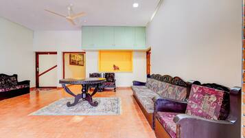 A spacious living room with a high ceiling, a ceiling fan, a dining table with chairs, a sofa set, and a patterned rug.