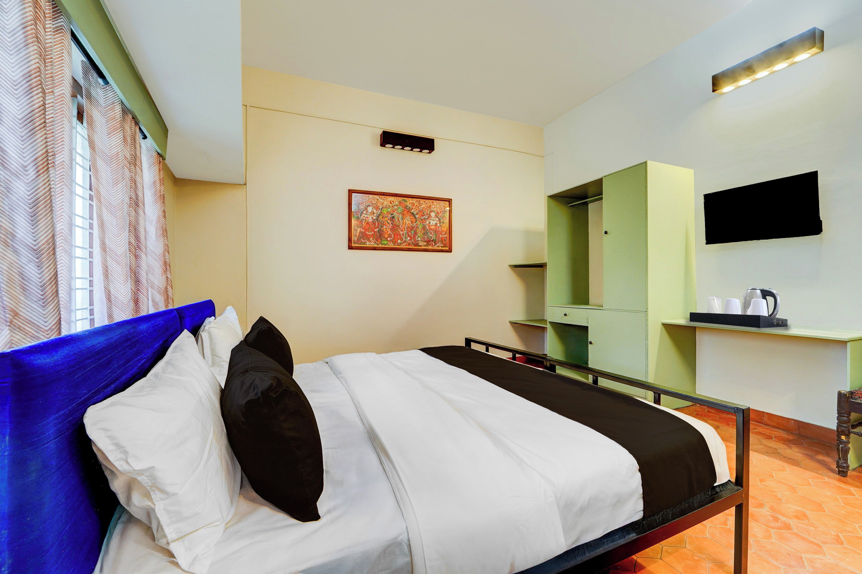 Una habitación de hotel con una cama, un cuadro en la pared, un televisor sobre la cama y un armario verde con espejo.