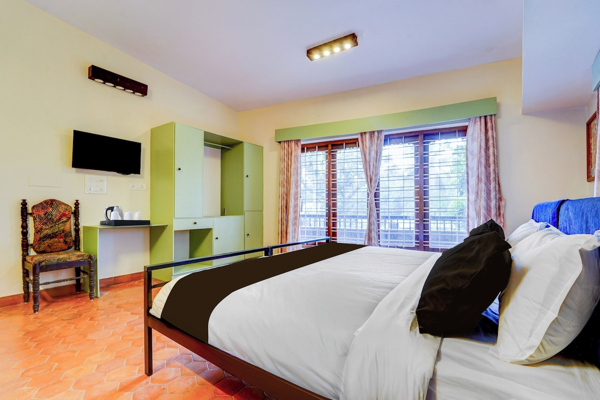 Habitación de hotel con cama, una silla, escritorio, televisor y ventana con cortinas.